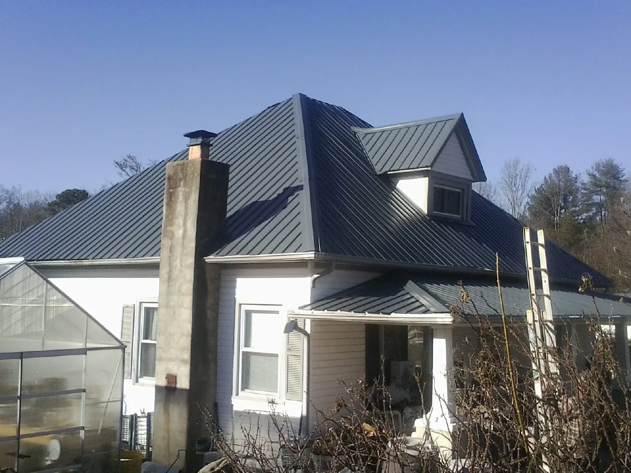 Dark blue standing seam metal roof on a white farmhouse with dormer — Slate & Tile Roof Repair by Roofing Brothers in North Windham