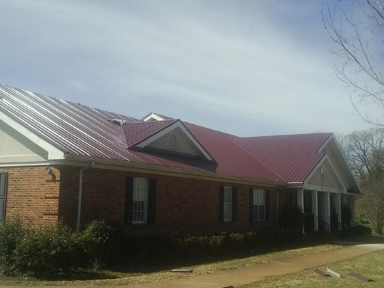 Red metal roof with gabled entries on a long brick building, from a Hail Damage Roof Repair job in North Windham