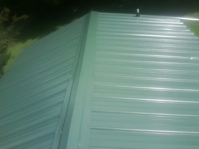 New green metal panels meeting at the ridge of a roof — Flat Roof Repair work by our crew in North Windham